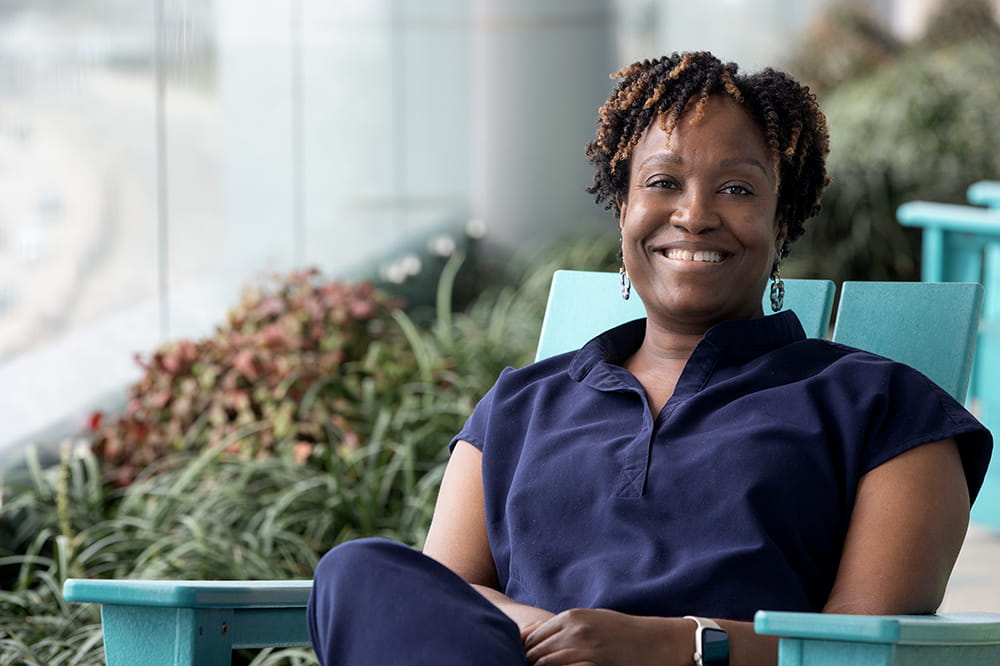 Woman in blue medical scrubs smiles while sitting in a chair.